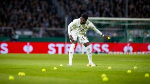 Alphonso Davies vom FC Bayern München befreit während des DFB-Pokalspiels bei Preussen Münster den Rasen von Tennisbällen. Diese hatten die Fans des deutschen Rekordmeisters aus Protest gegen den DFB aufs Feld geworfen.