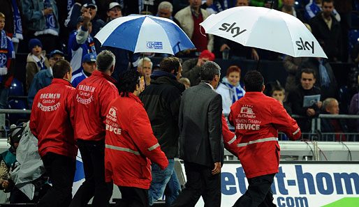 Geschützt von Regenschirmen und eigener Leibgarde verlässt Ex-Schiri Merk die Veltins Arena