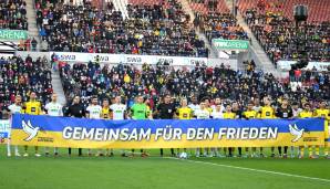 Dorsch und seine FCA-Kollegen halten gemeinsam mit den Spielern von Borussia Dortmund und dem Team von Schiedsrichter Deniz Aytekin ihre Friedensbotschaft in die Kameras.